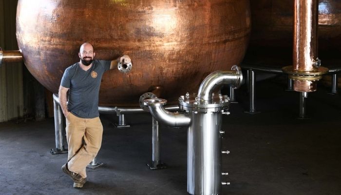 Chip Tate standing in front of his self-crafted copper pot still Chip Tate standing in front of his self-crafted copper pot still